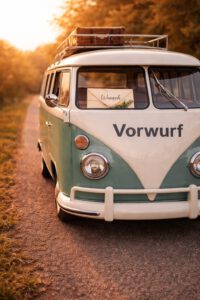 Alter VW-Bus im Sonnenuntergang mit der Aufschrift Vorwurf und einem Brief Wunsch hinter der Windschutzscheibe, Sinnbild für den Wunsch hinter jedem Vorwurf